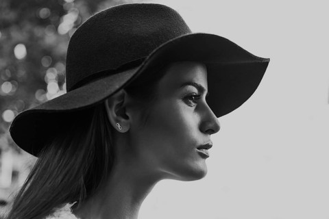 Black and white photo of a woman in profile wearing a wide-brimmed hat. The minimalist background