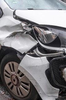 A heavily damaged white car after an accident. The front left mudguard is badly dented and