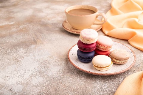 Macarons colourful cookies dessert, cup of coffee, on brown concrete background with orange linen