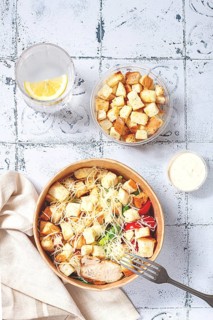 Caesar salad in a paper container, take it on the way, with sauce and croutons, on the table,