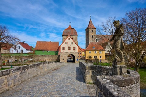 Stone bridge with statue and view of a village with church and historic buildings under blue sky,