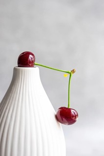 Ripe cherries balancing on a white ceramic vase against a modern, soft-focus background. The bright