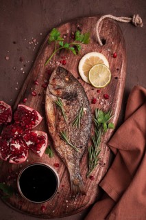 Fried dorado fish, with spices and herbs, on a wooden board, pomegranate sauce, close-up, no people