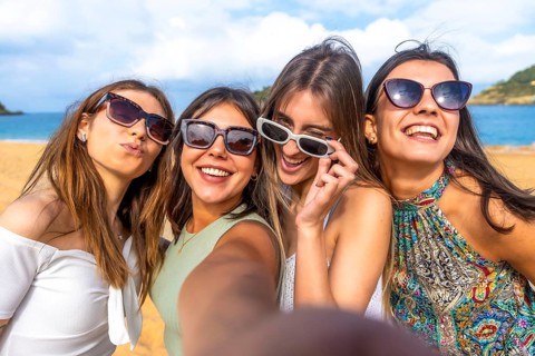 Four cheerful young women enjoying their summer beach vacation, smiling and posing for a close up