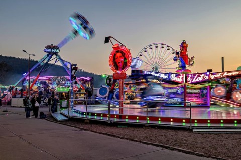 Colourful, illuminated fairground rides in full motion at dusk, carousel and the hustle and bustle