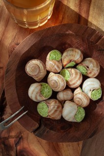 Snails cooked with herb oil on a wooden plate, served with white wine, natural light, no people