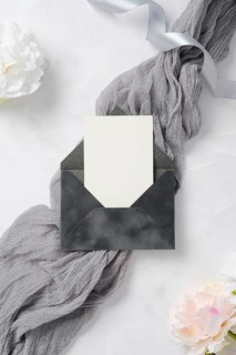 Elegant wedding card in an open envelope, placed on a soft gray fabric background. Accompanied by