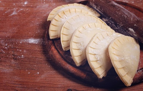 Raw chebureks, mini, on a cutting board, wooden table, close-up, no people