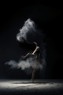 Brunette in black shorts and top jumping gracefully in a white dust cloud shot in dark room