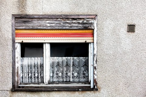 Old house facade, window with broken roller shutters and shabby curtains, Germany