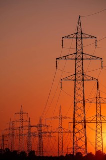 Silhouette of several high-voltage power lines and electricity pylons against a glowing orange and
