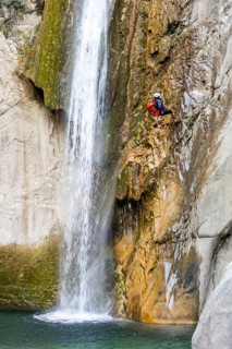 A canyoneer rappels down steep cliffs next to a waterfall, surrounded by breathtaking natural