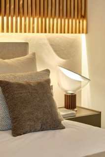 An elegant bedroom featuring a textured grey pillow, soft linen, a modern bedside lamp perched on a