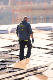 Worker walks on a solar roof, wearing work clothes, sunny, PV assembly at OBI hardware store,