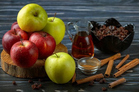Combination of apples, cinnamon sticks and raisins next to a glass carafe with rum