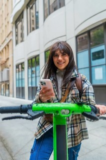 Woman standing on an electric scooter, navigating a city street and smiling at the camera while