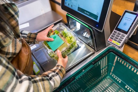 Woman using a self checkout machine, scanning a fresh salad in a plastic container at a grocery