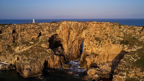 Drone shot, dramatic cliffs with lighthouse and sea in the background in daylight, morning light,