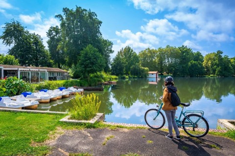 Woman with a backpack and bicycle standing by lake azur contemplating the calm water and pedal