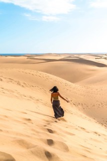 Tourist walking down the maspalomas dunes in gran canaria, spain, enjoying the sunny desert