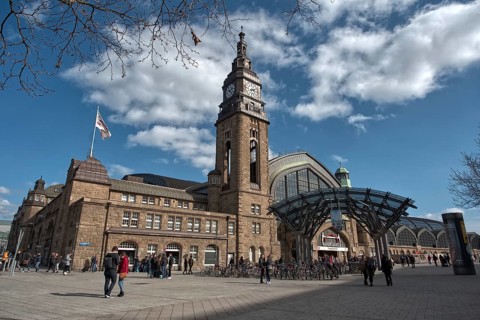Back side of Hamburger Bahnhof with clock tower, busy forecourt with people under a blue sky,