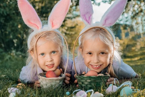 Two smiling children wearing bunny ears hold baskets filled with colorful Easter eggs, enjoying a