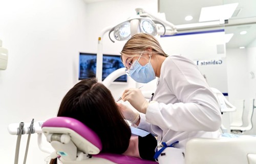 A dentist wearing protective gear attentively treats a patient in a modern dental clinic. The