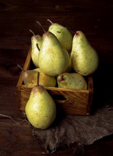 A rustic wooden box filled with fresh, ripe pears set against a dark wooden table. The natural