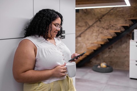 A young woman enjoys a break in a modern coworking space, holding a coffee mug and using her