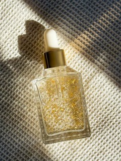 A transparent glass dropper cosmetic bottle filled with a luxurious serum containing gold flakes,