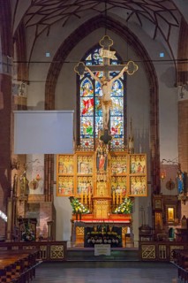 Gothic altar in a church, decorated with a crucifix and stained glass window in the background, St.