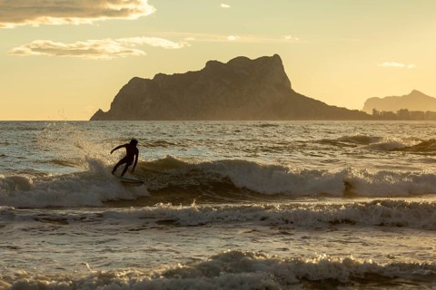 A surfer skillfully rides a wave as the warm hues of sunset cast a golden glow over the
