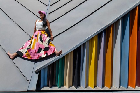 A woman in a vibrant, colorful outfit contrasts against a sleek modern architectural backdrop,