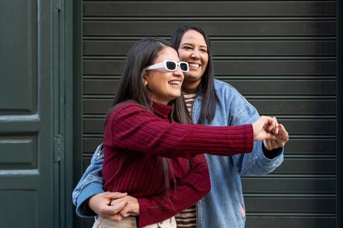 A cheerful Latin lesbian couple embraces and laughs in front of a green door, radiating joy and