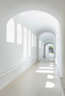 Sunlit corridor of hospital with arched windows creating playful light patterns. The minimalist