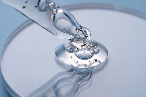 Macro shot of a transparent cosmetic dropper with serum and golden flakes floating, forming beads