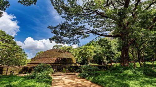 Ruins of an ancient stupa surrounded by lush greenery and a clear blue sky, temple ruins near