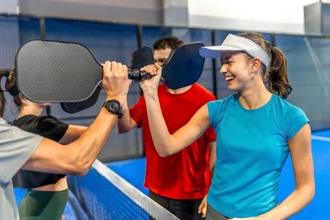 Group of diverse friends dressed in athletic apparel high fiving paddles over the net, celebrating