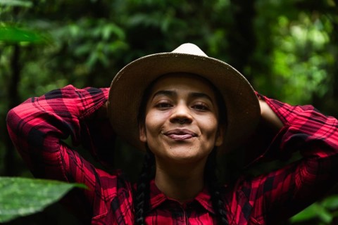 An Ecuadorian woman in a hat and plaid shirt enjoys nature in the lush Choco Andino rainforest of