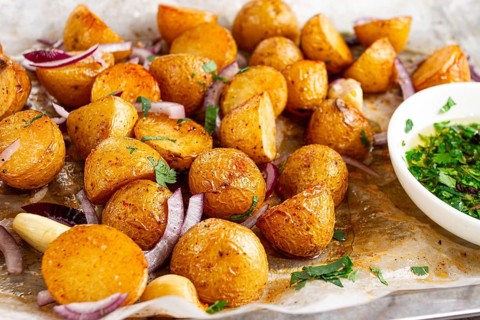 Roasted potatoes sit on a baking sheet next to chopped herbs and red onions. They are golden brown