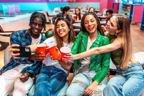 Four multi ethnic young friends are making a toast and taking a selfie at the bowling alley,
