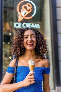 Vertical photo of a happy latin woman holding an ice cream cone outdoors next to the ice cream