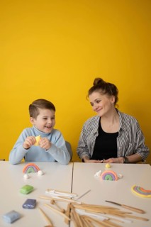 A child and a woman engage in a fun craft session, using colorful clay to create rainbows. The