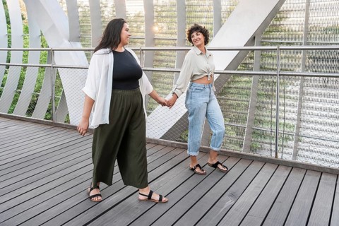 A joyful lesbian couple walks hand in hand on a modern bridge, with metal and wood elements,