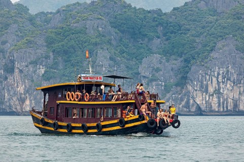 A traditional wooden boat with tourists sails through a rocky seascape, tourists on an excursion