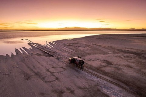 A stunning sunset casts a warm glow over Salinas Grandes, Salta, Argentina. An off-road vehicle is