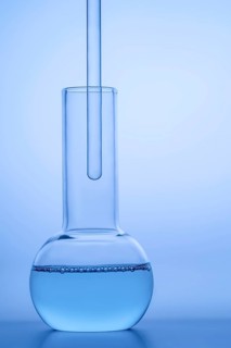 Close-up of a laboratory glass flask filled with blue liquid against a reflective blue surface,