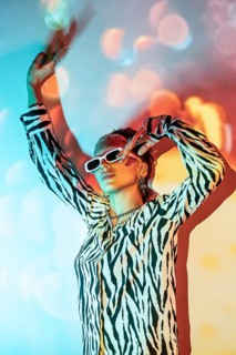Young trendy woman poses confidently, wearing bold zebra print and white sunglasses, with colorful