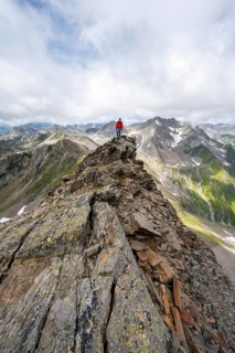 Mountaineer on a steep rocky ridge, at the summit of Lasörling, view of mountains of the Venediger