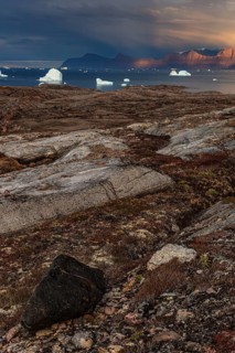 Evening light and atmosphere in fjord with icebergs in front of steep mountains, cloudy, autumn,